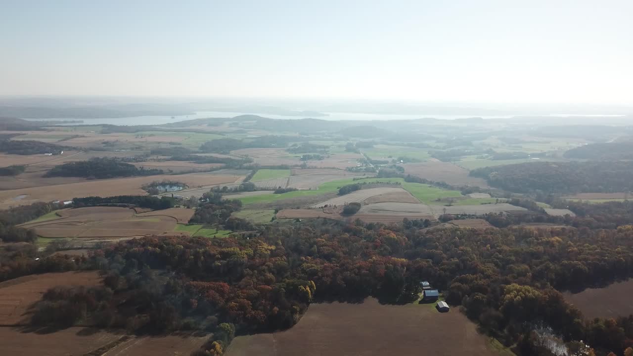 Expansive view of patchy farmland bordered by colorful autumn forest, with Lake Wisconsin gleaming on the distant horizon under bright, clear skies.