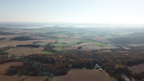 expansive view of patchy farmland bordered by colorful autumn forest, with lake wisconsin gleaming on the distant horizon under bright, clear skies.
