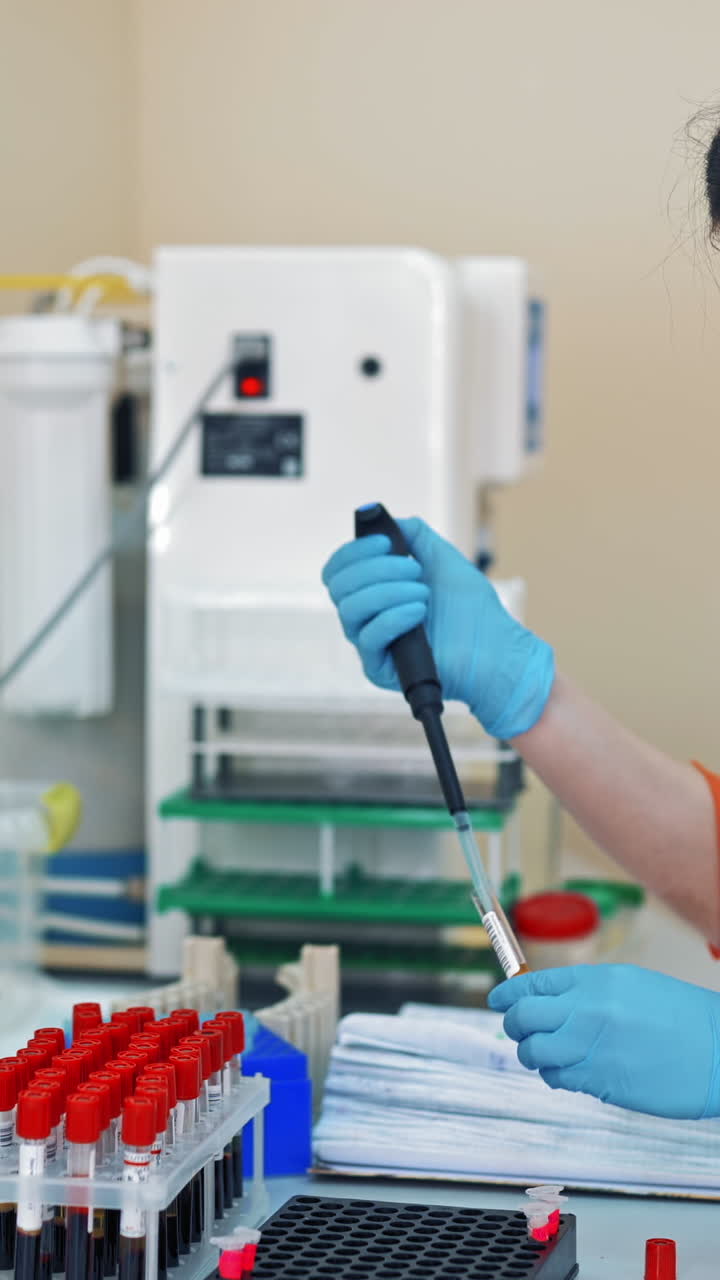 Beautiful laboratory technician woman in medical uniform works with blood samples. Female researcher is working with many vials of liquid in the laboratory. Vertical video