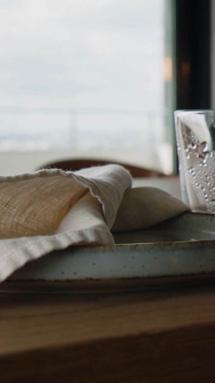 Vertical video: Panning camera revealing beige napkin on plate on table by window, glass entering