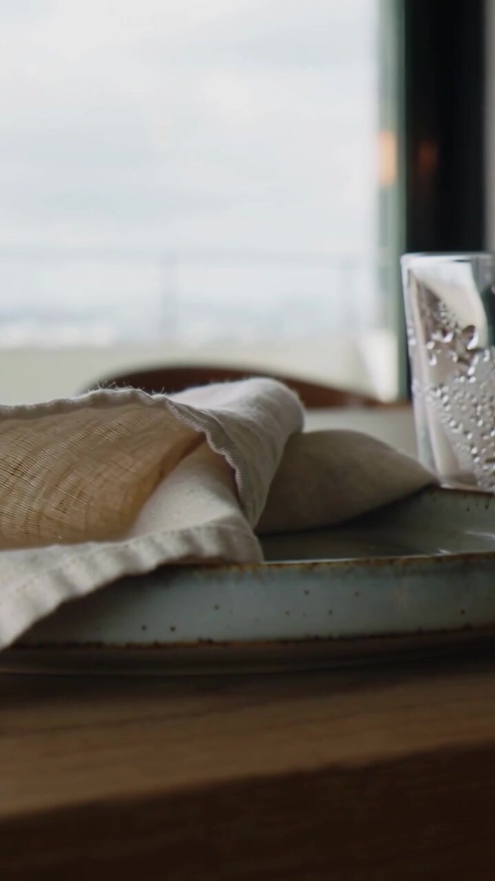 Vertical video: Panning camera revealing beige napkin on plate on table by window, glass entering
