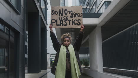 young american female activist holding a cardboard placard against the use of plastics during a climate change protest while looking at camera 1