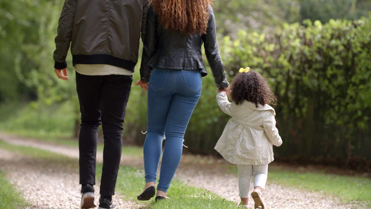 Coppia con la giovane figlia che cammina in una stradina di campagna, di spalle.