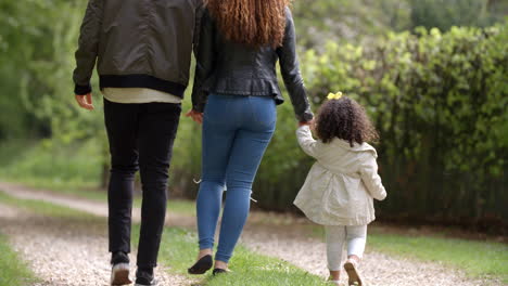 couple walk with young daughter in a country lane, back view