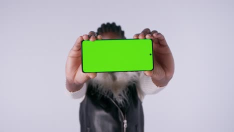 young woman holding her green screen smartphone and doing various hands movement in photo studio environment.