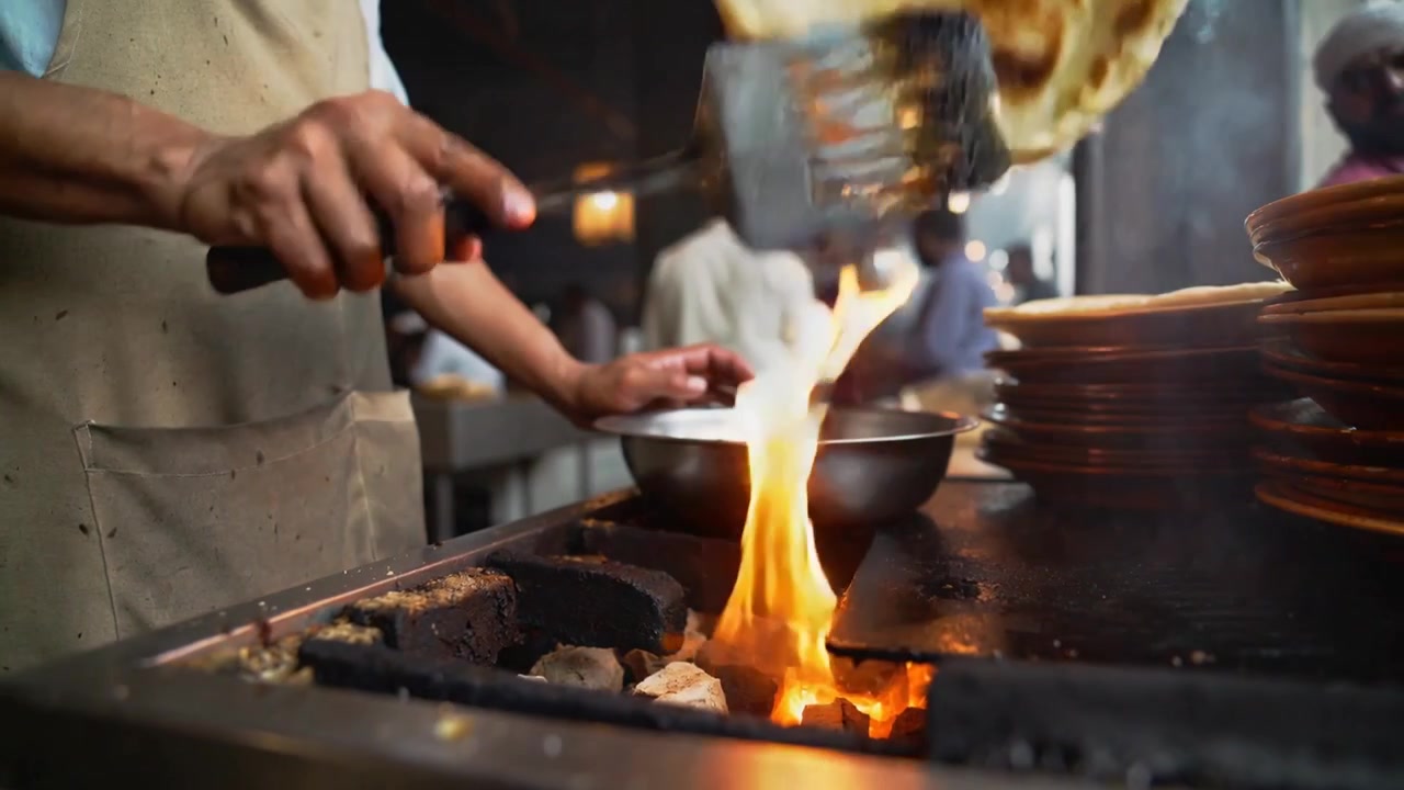 Placing naan on grill, cook in beige apron light-blue sleeves flipping bread with spatula to serve