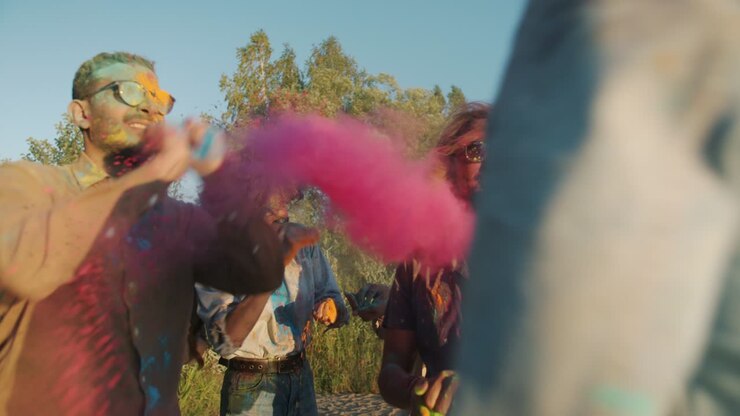 Slow motion of crazy young friends throwing powder paint and laughing dancing on beach on sunny day