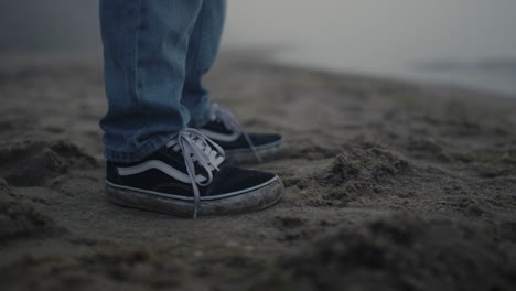 stylish guy sneakers standing sandy beach. man legs dancing on sea shore closeup