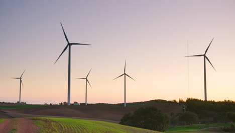 Stunning-sunset-silhouettes-wind-farm-over-grassy-countryside,-wide