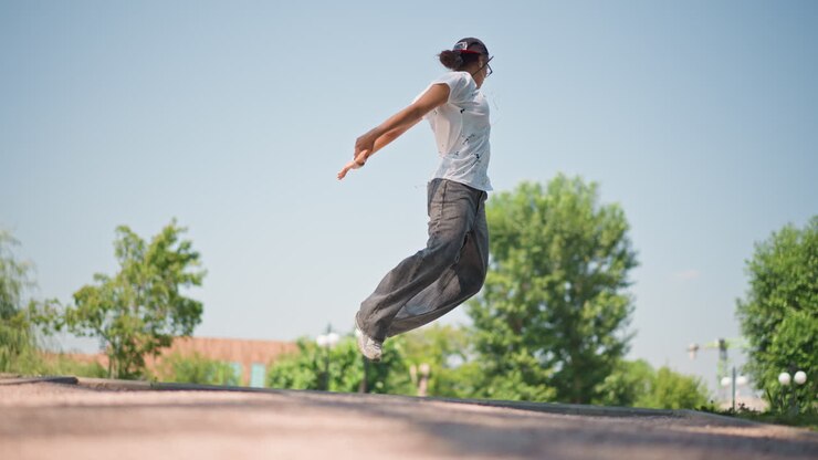Ballerino che si esibisce su un marciapiede illuminato dal sole, movimento a figura intera con cappello e borsa, artista di strada che prova il freestyle, routine atletica incentrata sul gioco di gambe e sull'equilibrio, coreografo che mette alla prova il groove