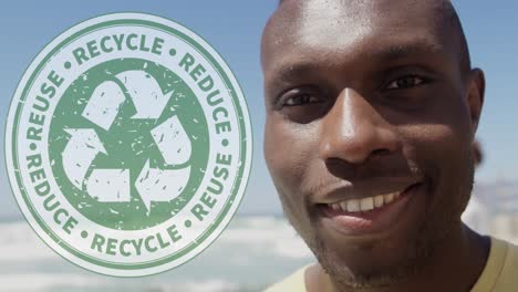 animation of recycling logo over portrait of smiling african american man at beach