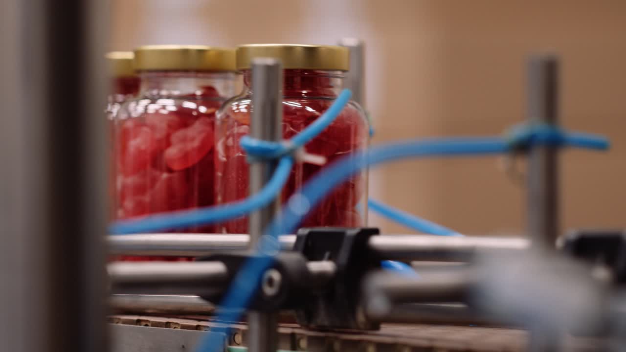 컨베이어 벨트에 빨간 젤리 비타민 보충제가 있는 병의 근접 추적