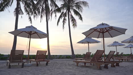 Silhouetted-Deckchairs-And-Parasols-With-Palm-Trees-In-The-Tropical-Beach-at-Sunset,-Inspirational-beach-resort-hotel