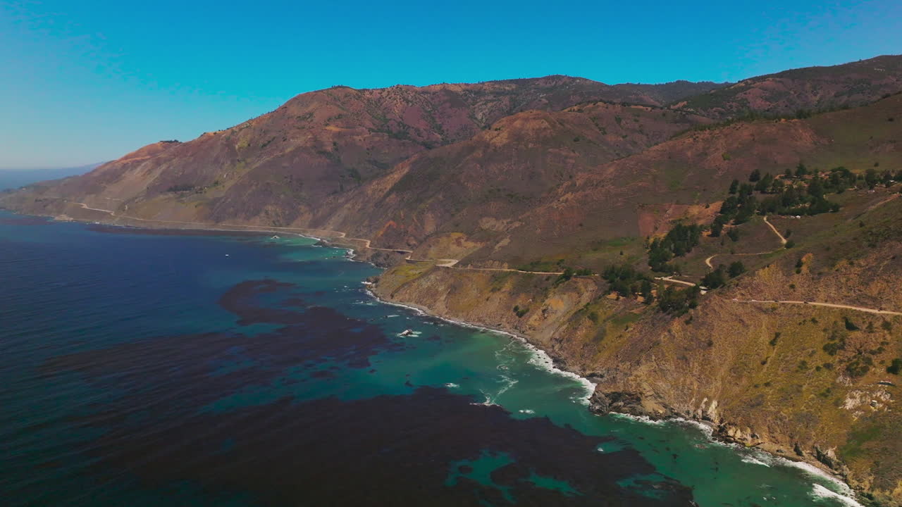 Rocks on the coastline of California. Beautiful dark blue water with algae bloom on surface. Sunny day footage from bird's eye view.