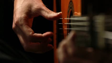 detalle de primer plano de las manos de un hombre tocando una guitarra clásica de madera con fondo negro