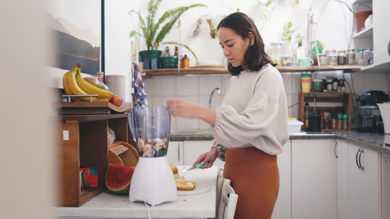 una mujer cortando frutas para hacer un batido en casa