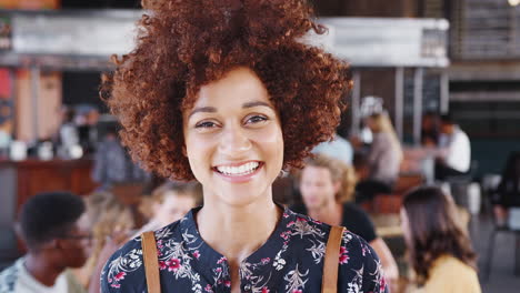 Portrait-Of-Waitress-In-Busy-Bar-Restaurant-Smiling-At-Camera