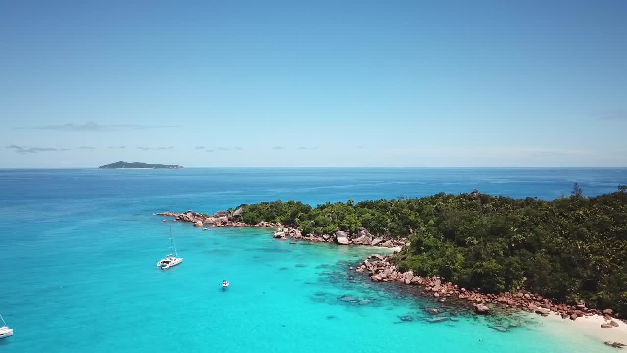Flying over beautiful turquoise bay on Seychelles island Praslin with boats on anchorage and panorama of the Indian Ocean