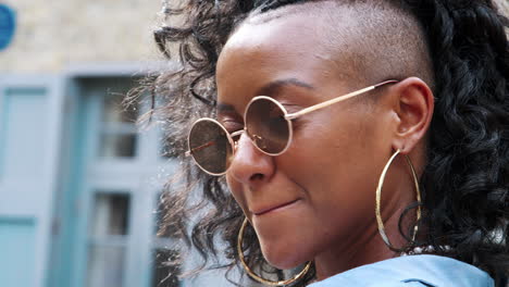 joven negra de moda con gafas de sol redondas volviéndose para mirar hacia la cámara, cabeza y hombros, de cerca