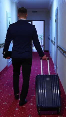 man in suit with suitcase in hotel. back view of a businessman with a trolley bag walking to his room in the hotel corridor. vertical video