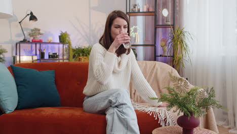 Thirsty-young-woman-sitting-at-home-holding-glass-of-natural-aqua-make-sips-drinking-still-water