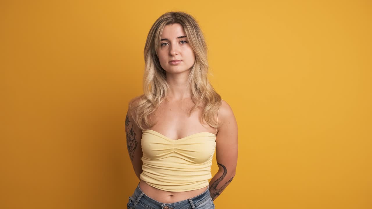 Serious young woman standing with hands behind on yellow background