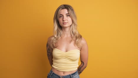 serious young woman standing with hands behind on yellow background