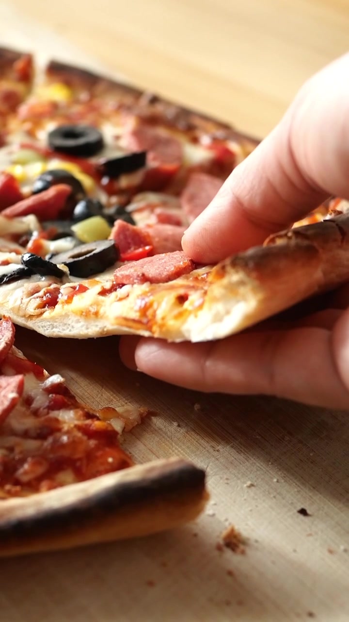 Mano che prende una deliziosa fetta di pizza con salame piccante e olive
