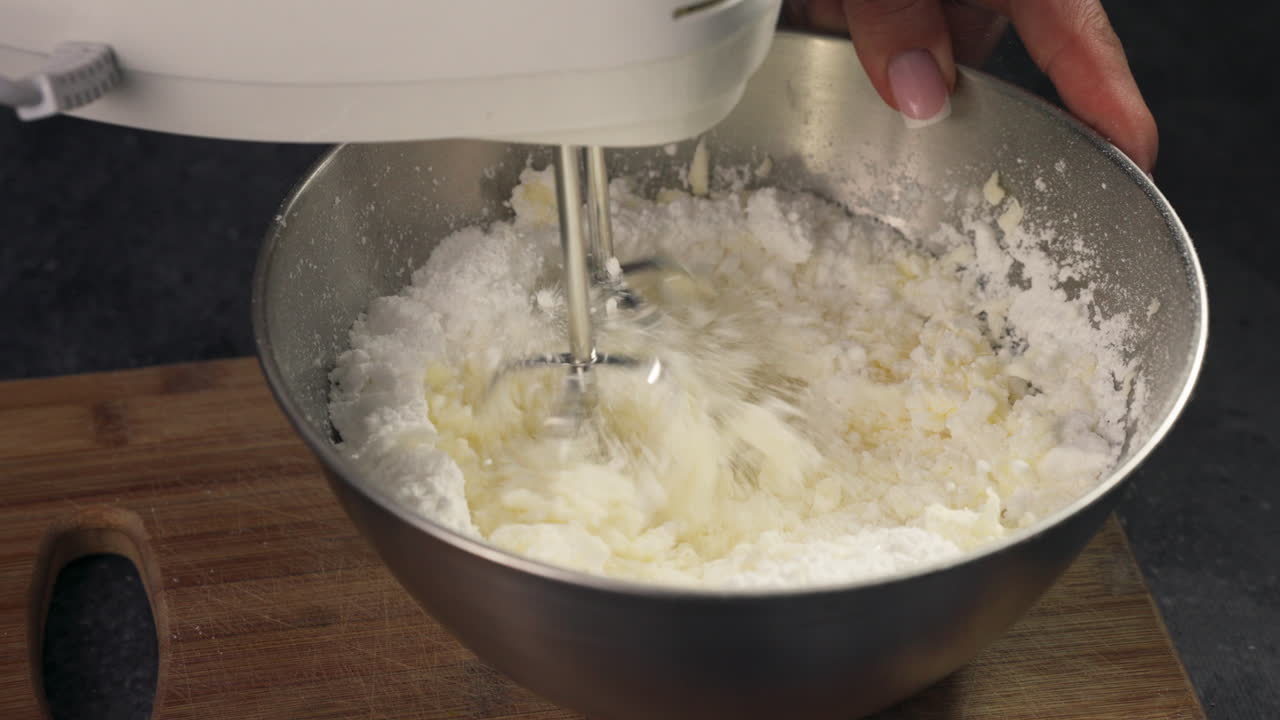 Creamy frosting being whipped for cupcakes in a stainless steel mixing bowl using hand mixer