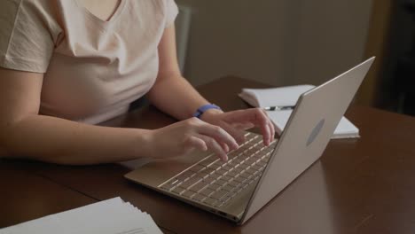 female hands are typing text on laptop keyboard. fingers quickly press the keys on the keyboard. there is notebook next to it. personal computer, remote work at home, business, study, messaging, chat