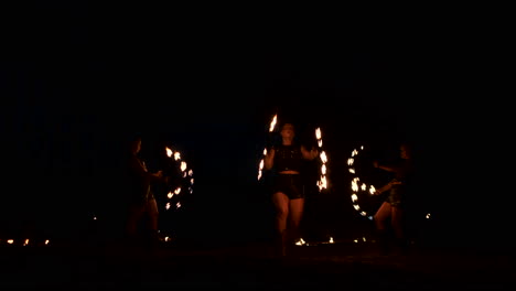 Slow-motion:-Professional-fire-performance-three-women-in-dripping-clothes-dance-and-spin-with-flaming-torches-and-a-man-with-flamethrowers-in-the-background.