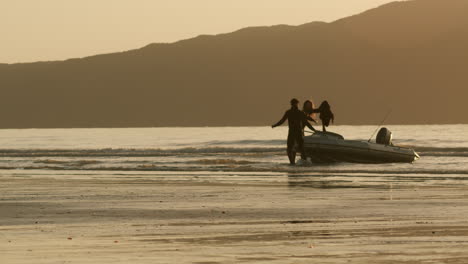 couple launching inflatable boat at sunset beach