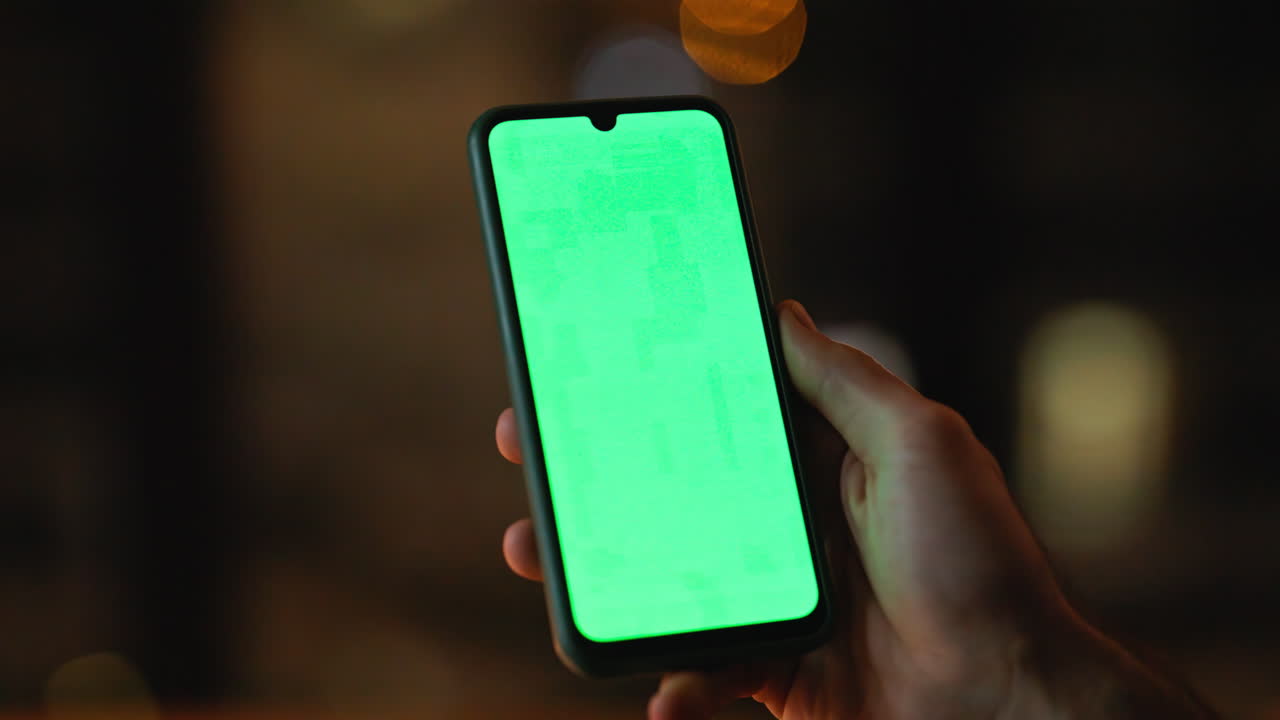 Guy hand holding green screen smartphone at night apartment closeup. Unknown man