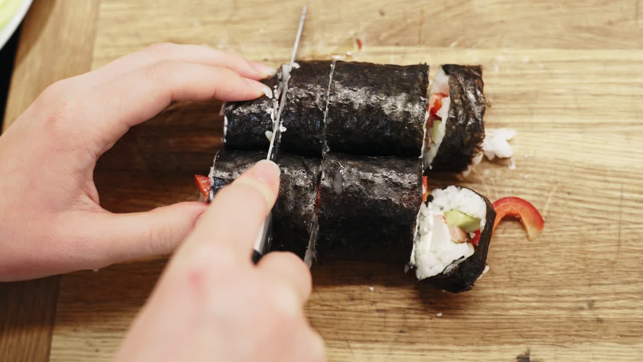 primer plano de ángulo alto de manos cortando sushi nori en trozos pequeños con un cuchillo
