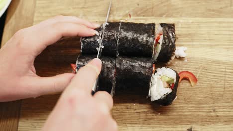 Nahaufnahme-Der-Hände,-Die-Nori-Sushi-Mit-Einem-Messer-In-Kleine-Stücke-Schneiden