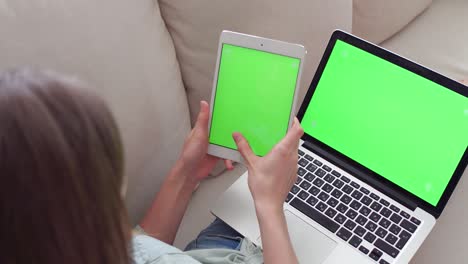 hermosa chica usando una tableta pc y una computadora portátil con pantalla verde pre-enclavada sentada en el sofá en casa.