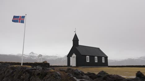 black church of budir and flag of iceland in foggy mountain landscape