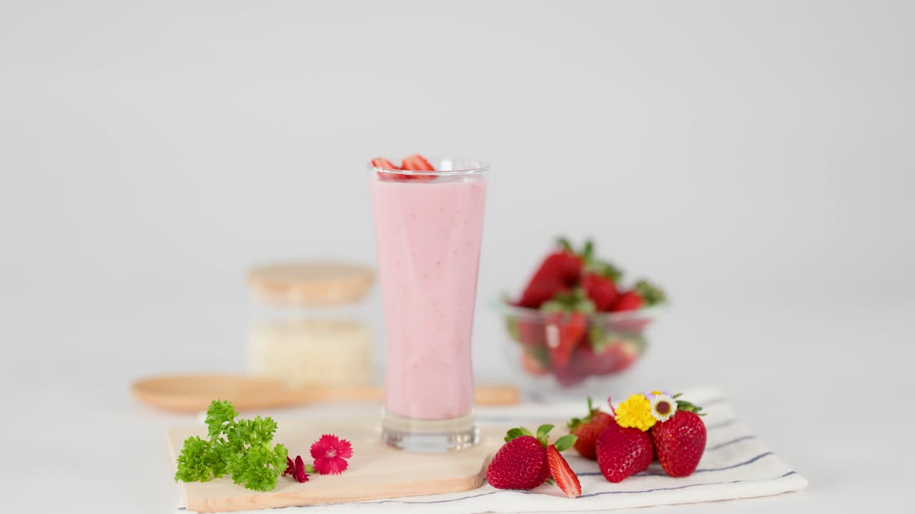 Una mano inserisce una cannuccia rossa a spirale in un cremoso milkshake alla fragola rosa, illuminazione luminosa da studio, sfondo bianco