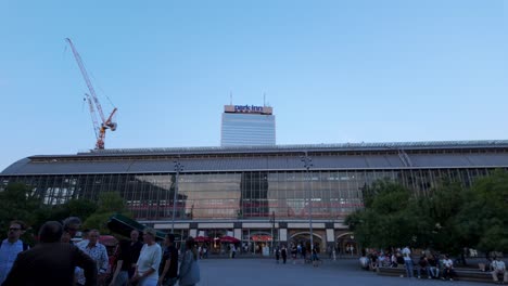a wide-angle video shot during ifa in berlin, featuring people walking in front of a large glass building with a tilt-up camera movement, revealing the park inn hotel and construction cranes above