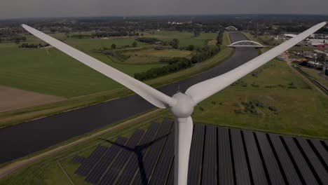 closeup aerial of wind turbine blades and solar panels in the netherlands dutch flat landscape with twentekanaal and bridges in the background