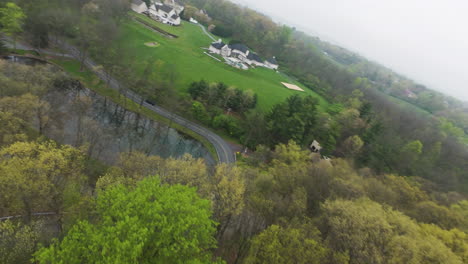 drone flight over forest trees in upscale suburb district of american town with pond and villas during foggy day