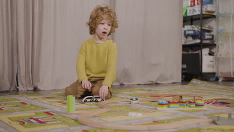 niño rubio jugando con coches de madera en la alfombra en el aula en una escuela montessori