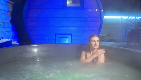 happy relaxed long-haired woman sits in jacuzzi. lady in stripy swimsuit enjoys water in hot tub.
