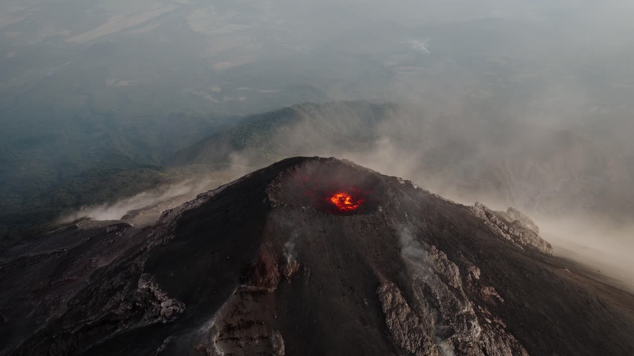 Slow orbit aerial of Fuego Volcano crater with glowing lava and steam drifting over the surrounding Guatemalan terrain