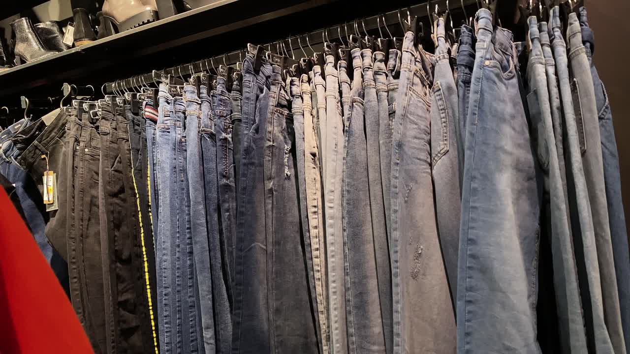 Denim pants hang on hangers in the store, the girl goes past the hangers in the clothing store