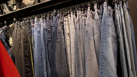 denim pants hang on hangers in the store, the girl goes past the hangers in the clothing store
