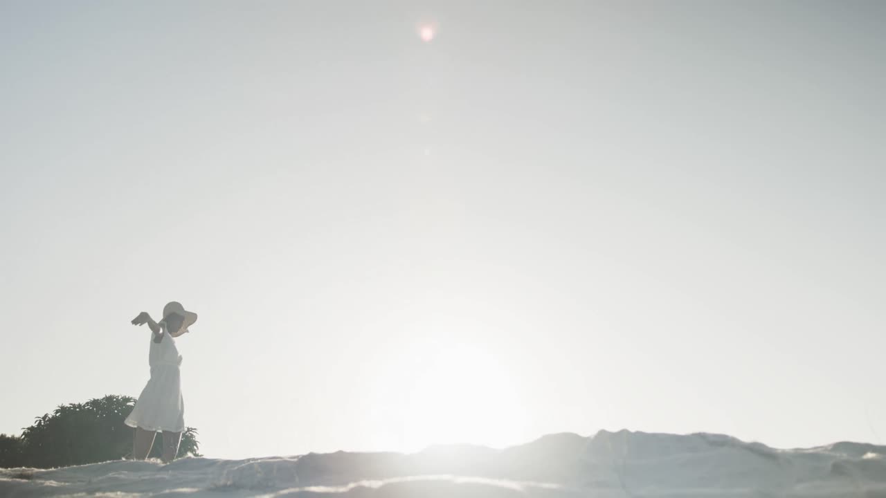 해변에서 뒷빛으로 춤을 추는 선드레스와 선을 입은 행복한 두 인종 여성, 느린 동작