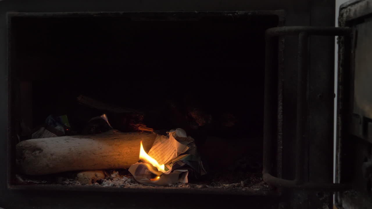 Male hand lights a piece of paper in a wood stove