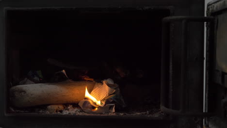 male hand lights a piece of paper in a wood stove