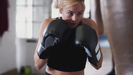 female boxer in gym training with old fashioned leather punch bag